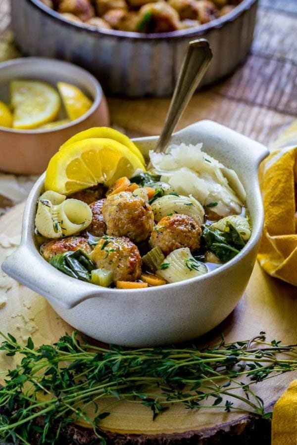 A single serving of Noodle Soup with meatballs with garnishes of lemon slices and shaved Parmesan.