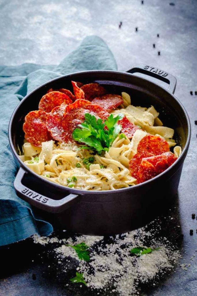 Lemon Pasta with Crispy Salami in a black Staub cocotte on a rustic blue table top.
