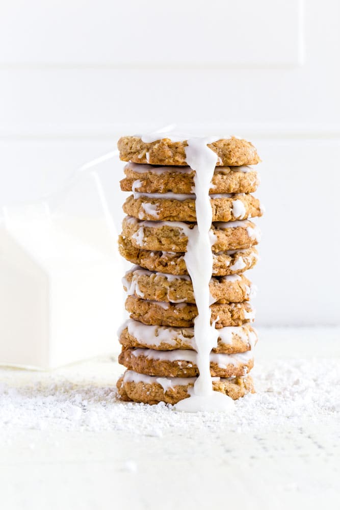 A stack of iced oatmeal cookies with a glass carton of milk and straw.