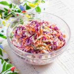 Coleslaw in a clear glass serving bowl on a white farmhouse table.