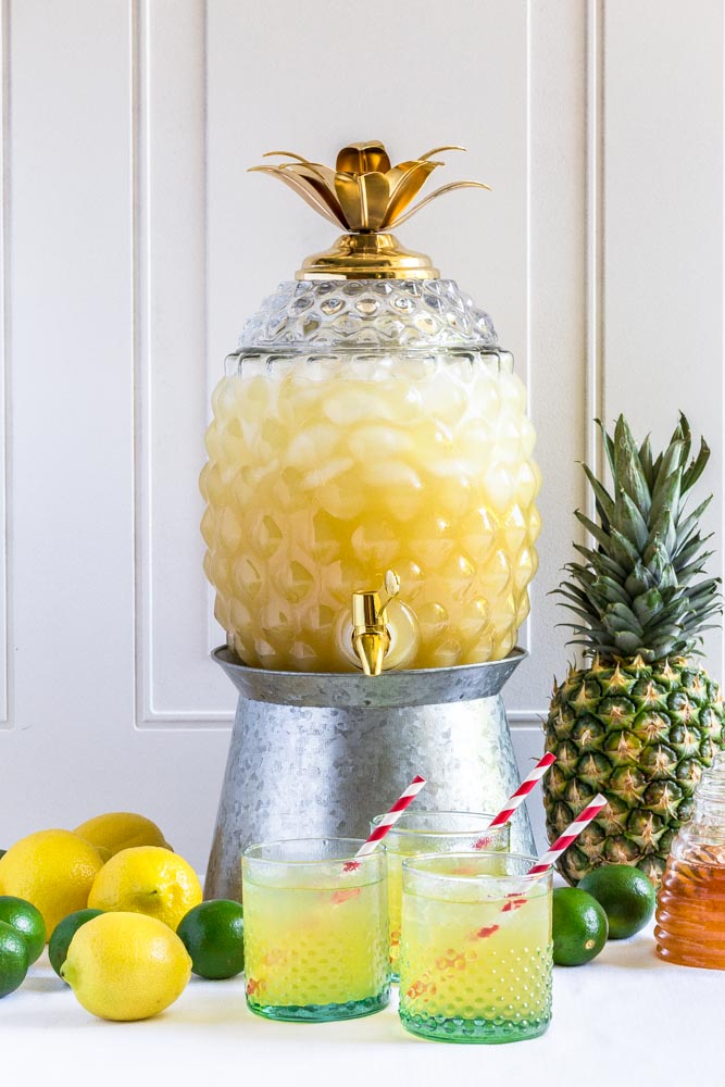 Pineapple fruit punch served in a pineapple-shaped glass jar container on a beverage stand.