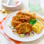 Schnitzel sprinkled with minced parsley, served on a round white plate with lemon wedges.