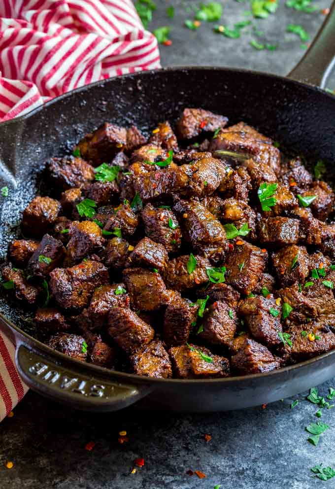 Garlic butter steak bites in a black cast iron pan garnishes with fresh parsley and red pepper flakes.