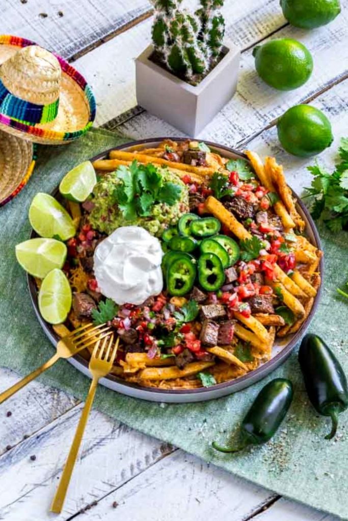Mexican carne asada fries on a Cinco de Mayo table decorated with mini sombreros.