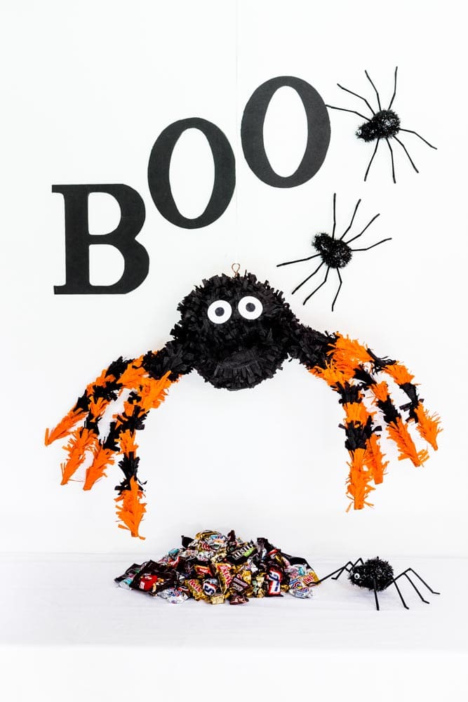 A DIY Spider Pinata made from paper mache hanging above a pile of Halloween candy.