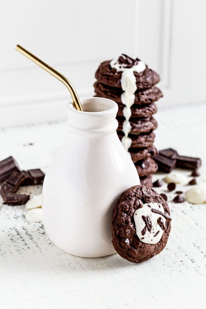 A ceramic milk bottle next to a stack of triple chocolate cookies.