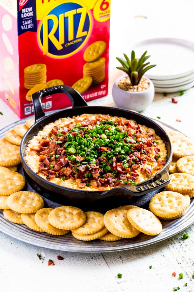 Loaded cream cheese dip garnished with bacon and green onions, served with butter crackers.