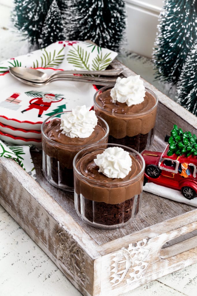 Three glass cups featuring chocolate pudding dessert with a dollop of whipped cream on top.