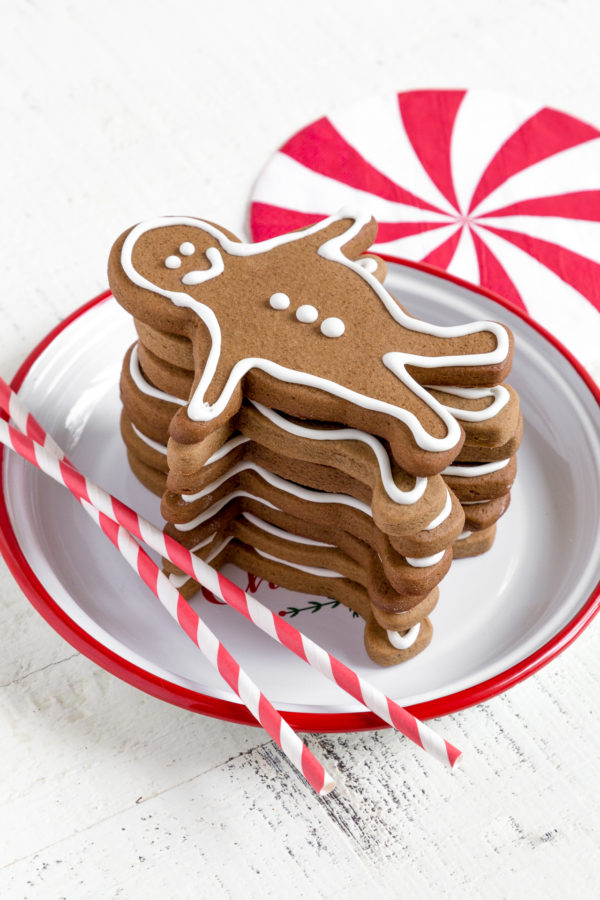 A stack of gingerbread men on a white and red plate next to red-and-white striped drinking straws.
