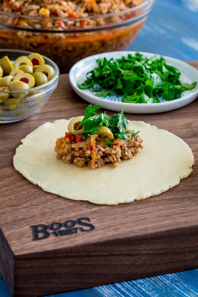 Assembly of a beef empanada on a Boos wooden cutting board.