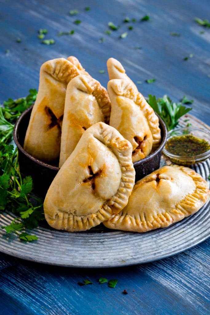 Traditional Argentinian empanadas served on a rustic metal tray with chimichurri sauce.