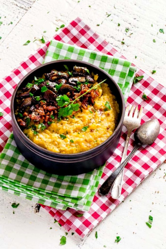 Cheesy Mushroom Polenta with bacon in a bowl next to a spoon and fork.