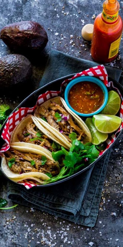 Carnitas Tacos served in a rustic metal food tray with fresh slices of lime.