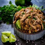 Instant Pot Pork Carnitas served in a rustic metal bowl with limes and cilantro.