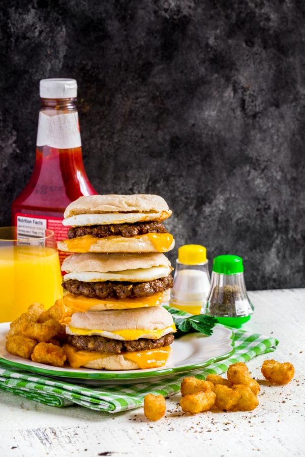 A stack of three sausage egg mcmuffin breakfast sandwiches on a plate.