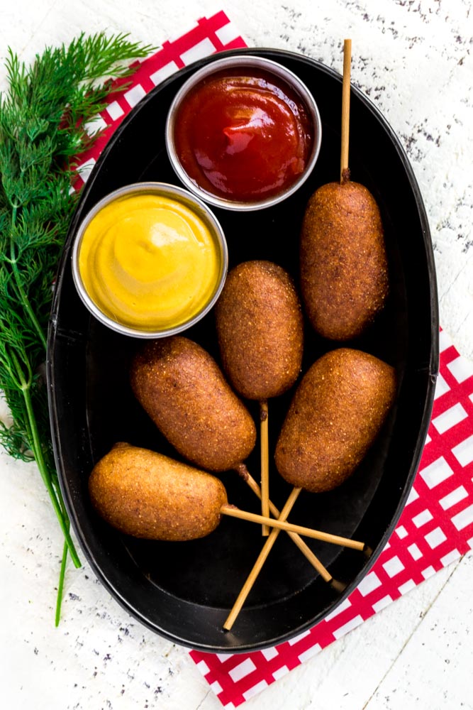 5 mini corn dogs in a serving basket with mustard and ketchup.