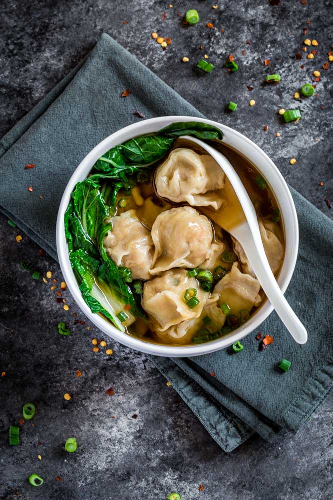 An individual serving of wonton soup with Chinese dumplings, broth, bok choy and sliced green onion.
