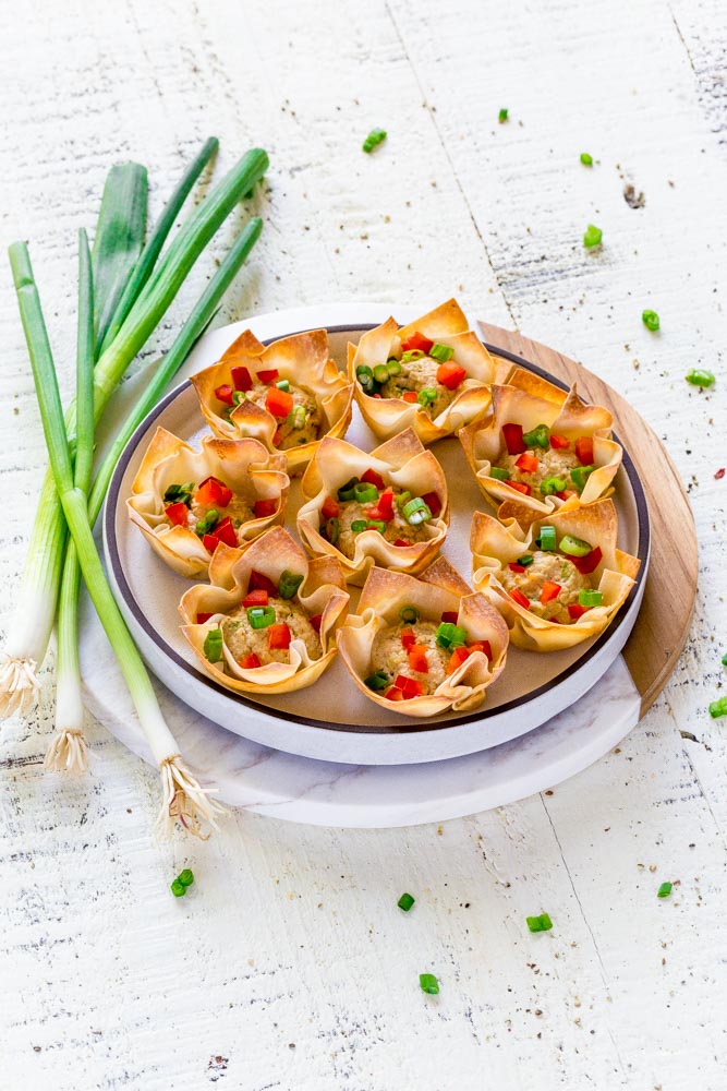 Crab rangoon a round serving platter next to a small bunch of fresh green onions.