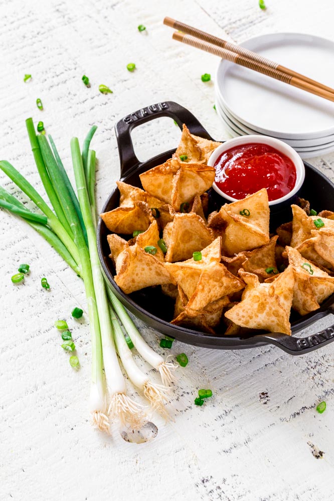 Sweet cream cheese wontons in a round black serving dish with sweet and sour sauce.