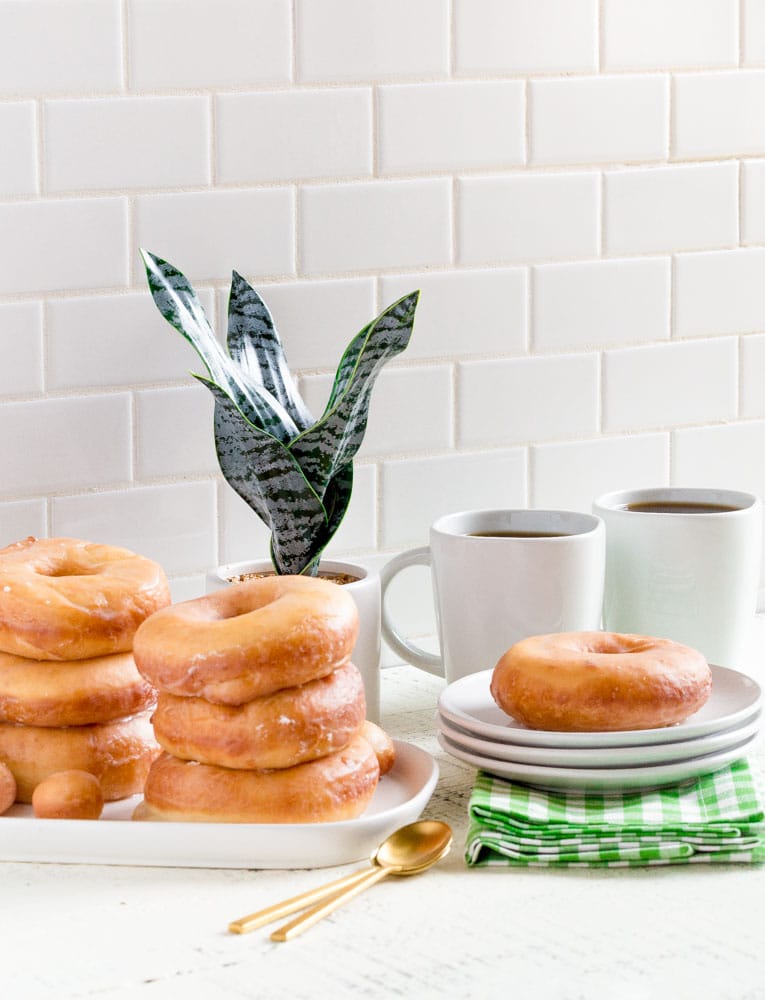 Glazed donut on a plate next to a full platter of vertically-stacked homemade donuts