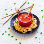 Chinese sweet and sour sauce served in a clear glass bowl alongside crispy wonton strips.