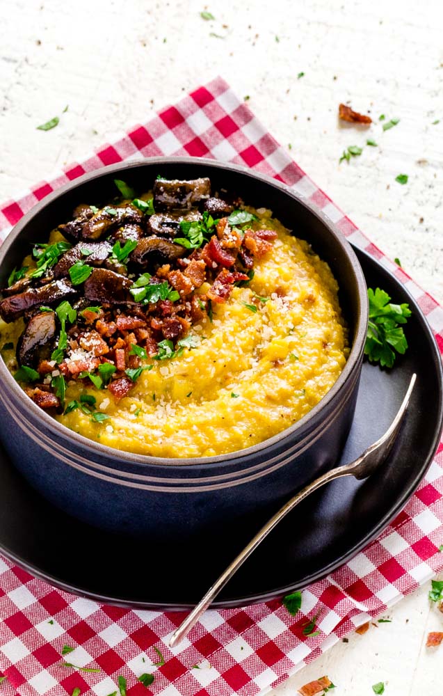 Cheesy Mushroom Polenta with Bacon served in a bowl on top of a plate with spoon.