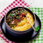 Cheesy Mushroom Polenta with Bacon served in a dark-brown bowl with a metal fork.