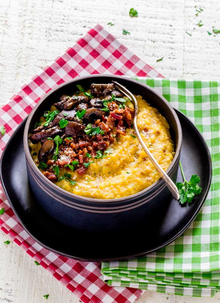 Cheesy Mushroom Polenta with Bacon served in a dark-brown bowl with a metal fork.