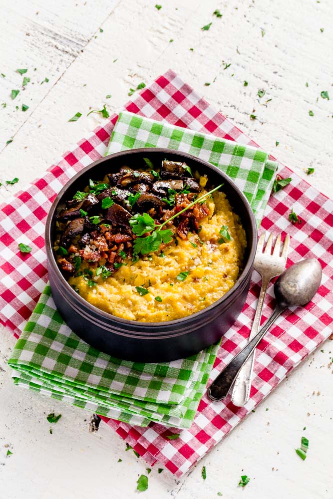 Cheesy polenta in a bowl topped with oven roasted mushrooms, parsley and bacon bits.