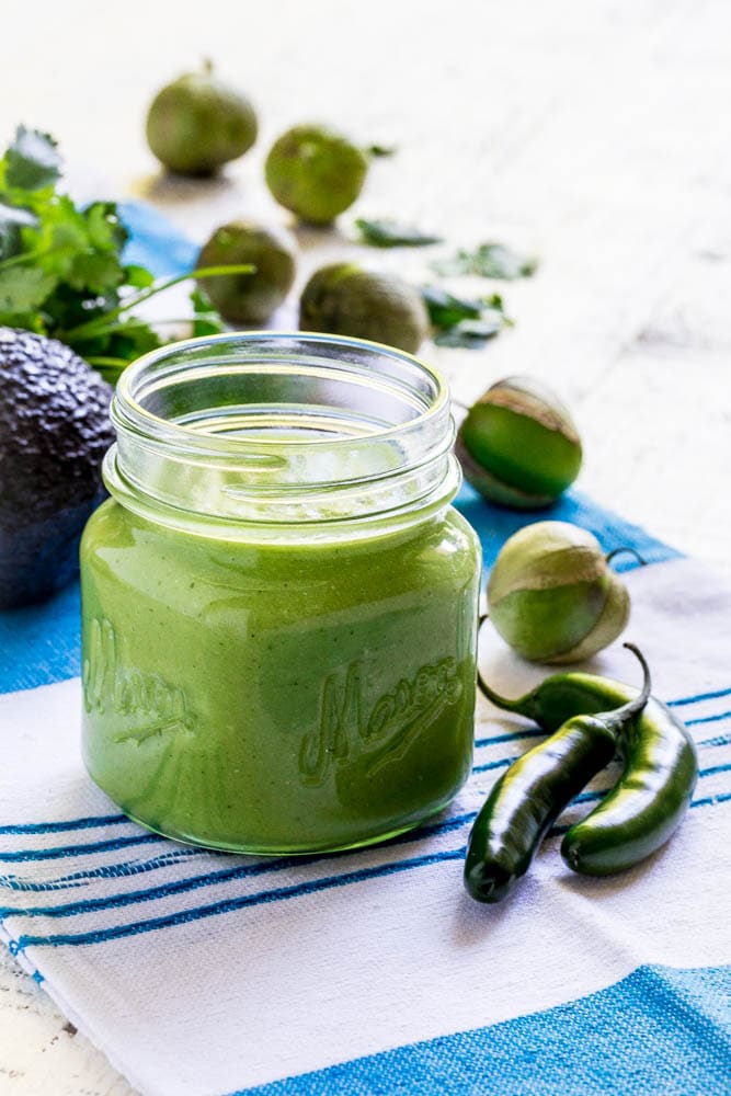 Salsa verde in a mason jar next to raw ingredients for green salsa.