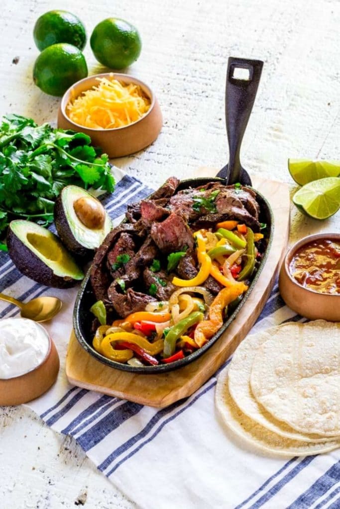Pinterest graphic for easy steak fajitas served in a sizzling cast-iron platter with veggies.