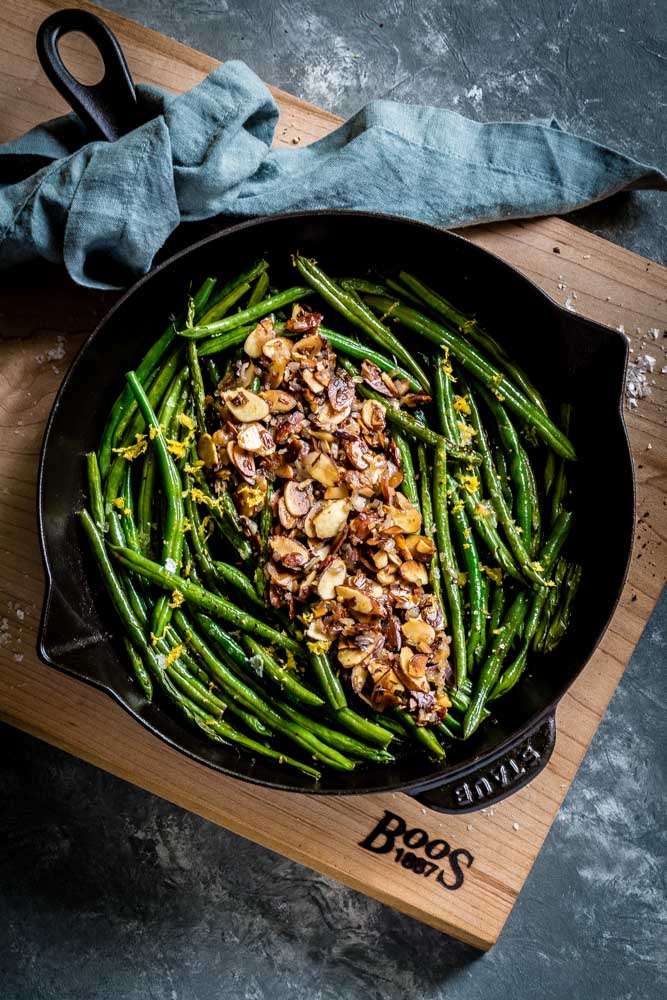 Green Beans Almondine served in a black skillet seated on a wooden maple board.