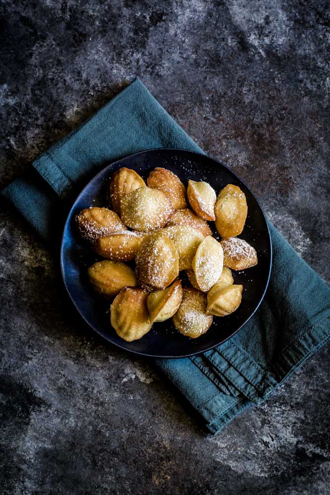 French Madeleine Cookies in a dark bowl sitting on a deep blue napkin.