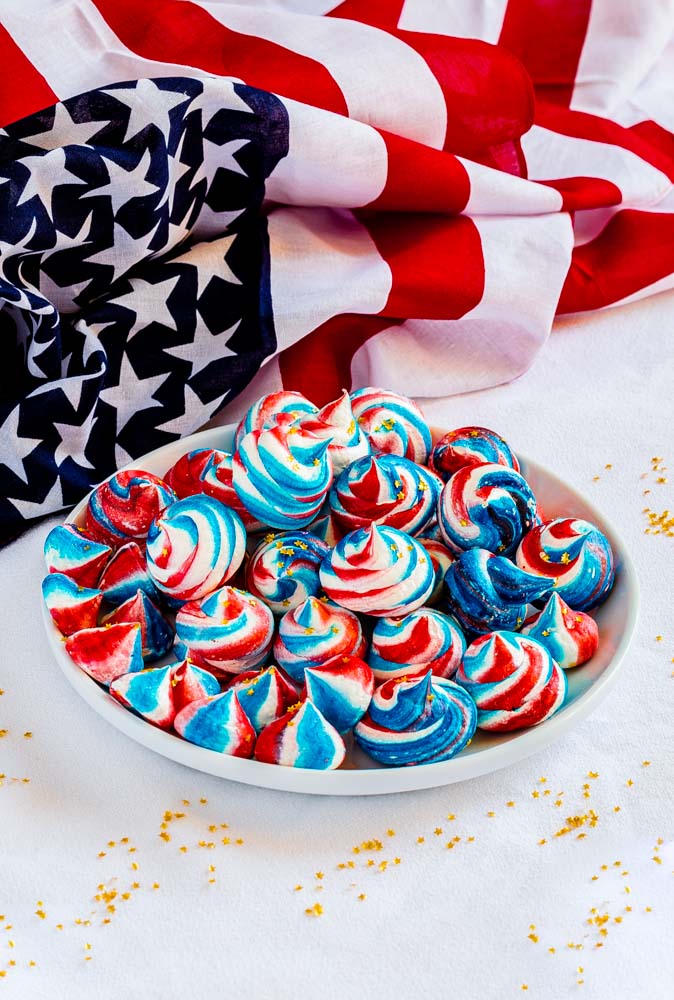 A small plate of red, white and blue cookies next to an American flag.
