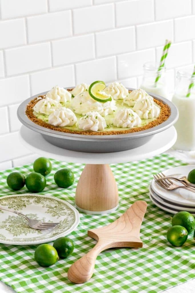 Grandma's favorite key lime pie served on a wooden cake stand next to dessert plates and forks.