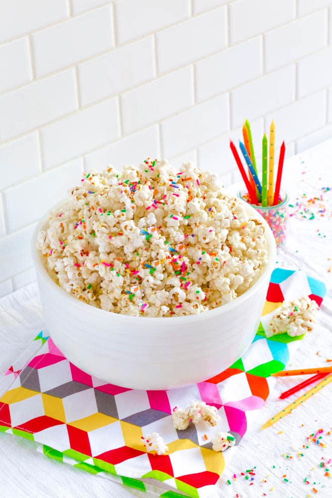 Birthday Cake Popcorn in a white bowl next to bright colorful birthday candles.