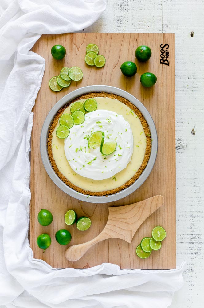 A fresh Key lime pie garnished with whipped cream and lime zest with a wooden pie server.