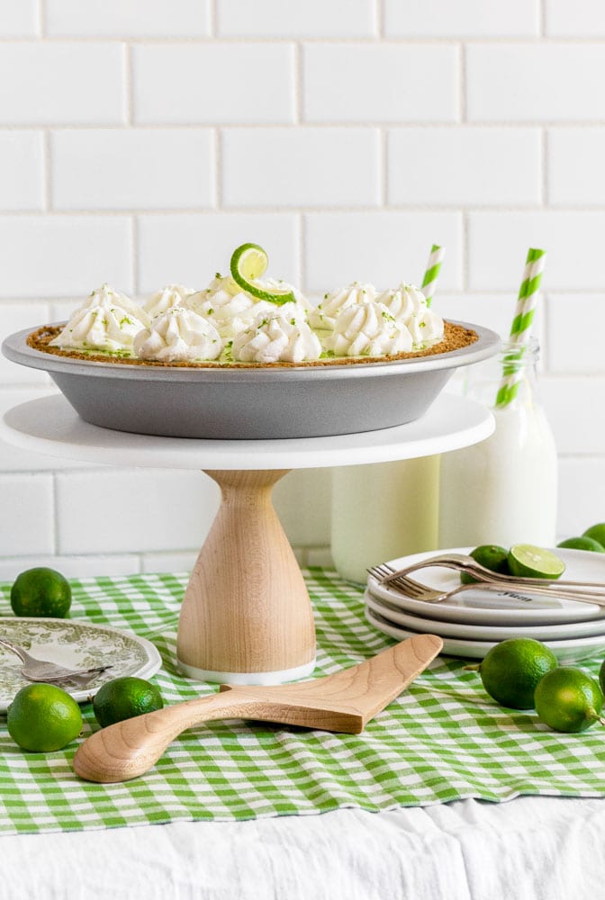 A homemade Key lime pie displayed on a wooden cake stand on a dessert table.
