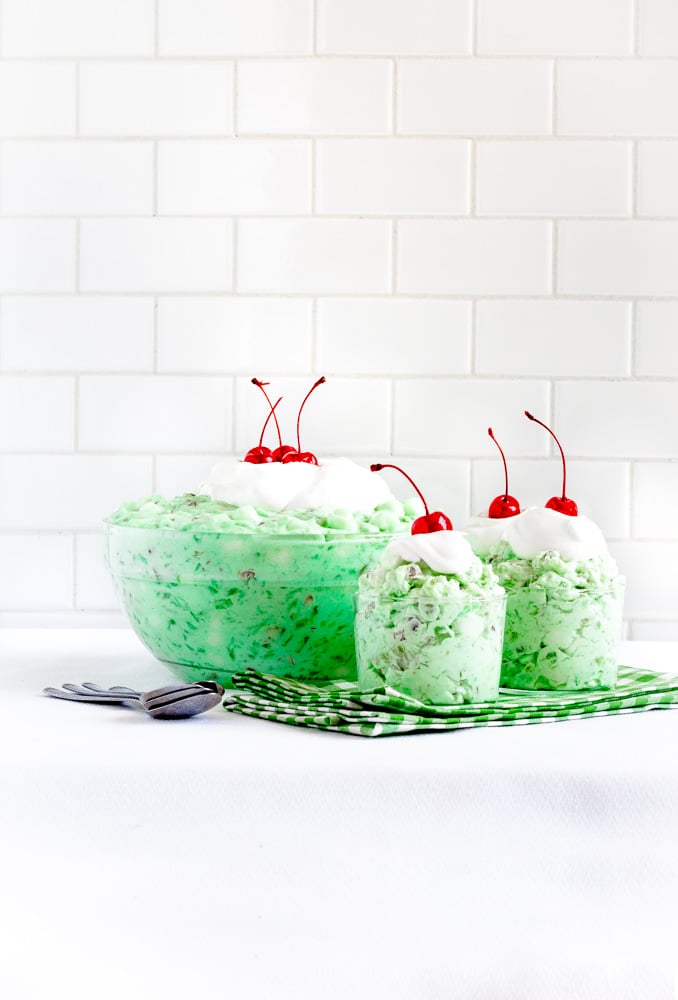 Pistachio Watergate Salad in dessert cups and a large glass bowl on a white tabletop.