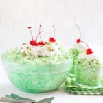 Watergate salad in a glass serving bowl with dessert dishes and spoons on the side.