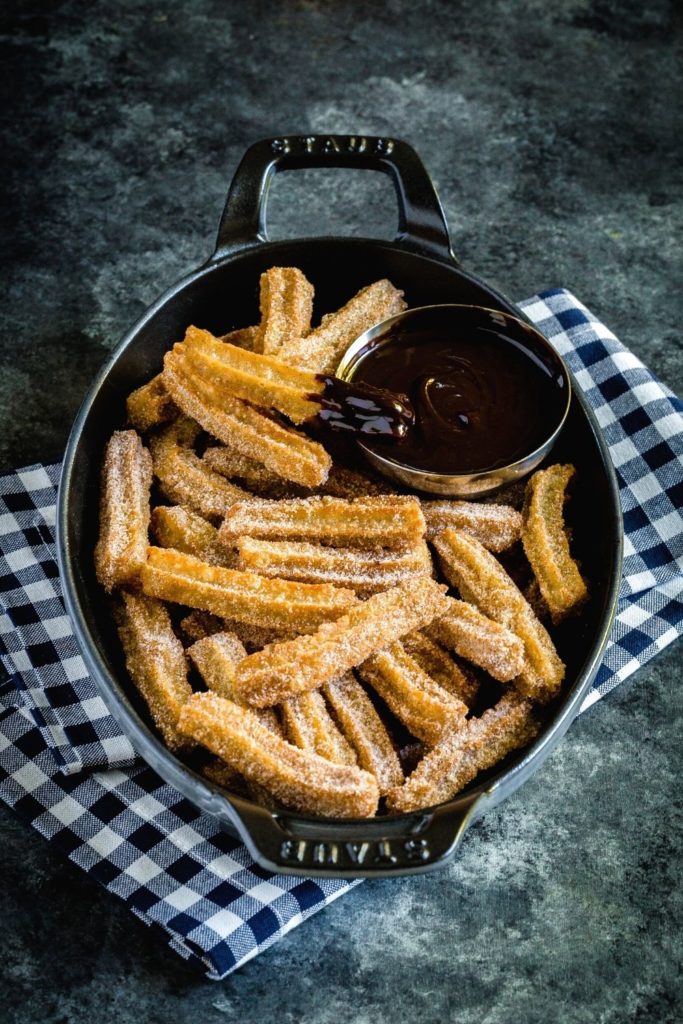 Freshly-made Mexican churros served in an oblong cast iron dish with chocolate dipping sauce.
