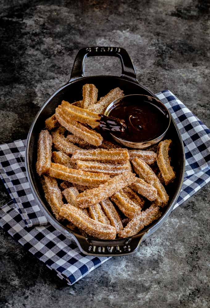 Mexican churros served in a black cast iron dish with chocolate sauce for dipping.