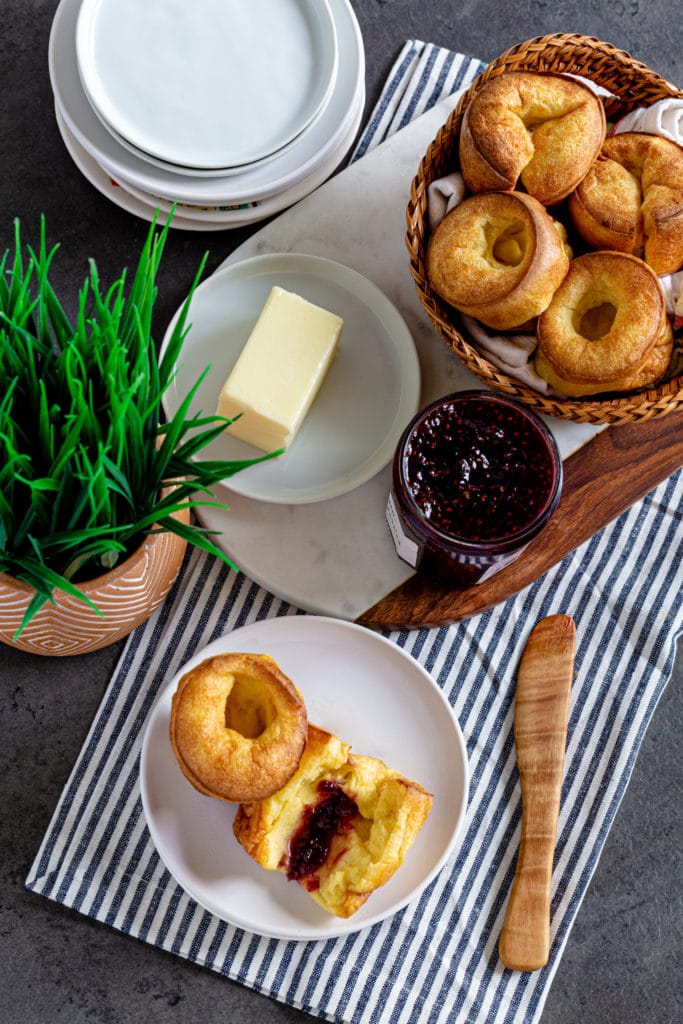 Overhead view of a breakfast bar with popovers, plates, butter and jam, and a small plant.