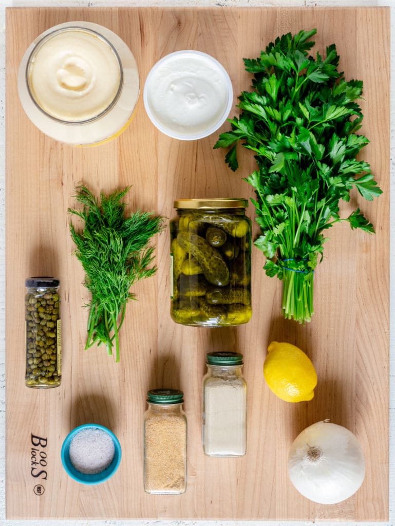 Ingredients for tartar sauce recipe laid out on a large wooden board.