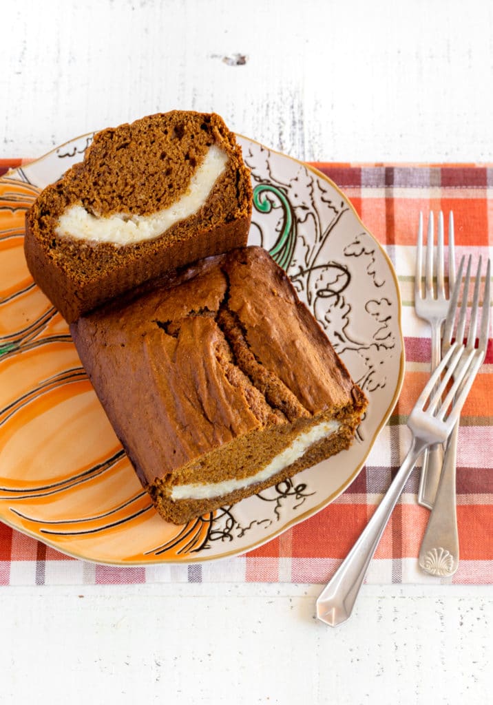 A loaf of pumpkin bread cut in half so you can see the cream cheese swirl inside.