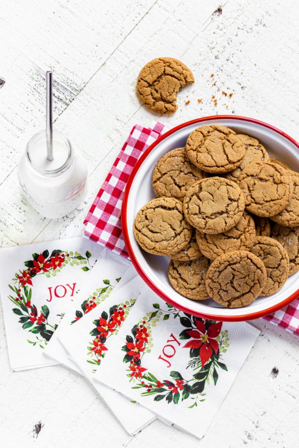 Overhead view of a plate of ginger snap cookies with milk and holiday napkins.
