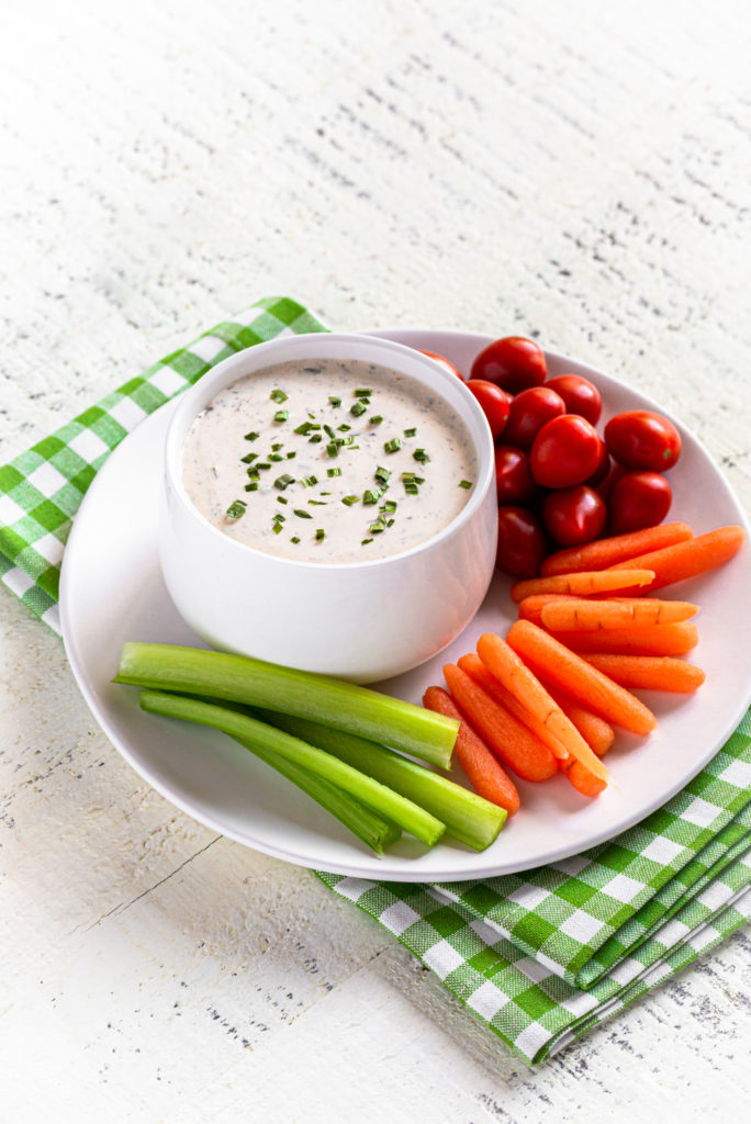 Buttermilk Ranch Dressing garnished with chives, served with baby carrots, celery sticks and baby tomatoes.