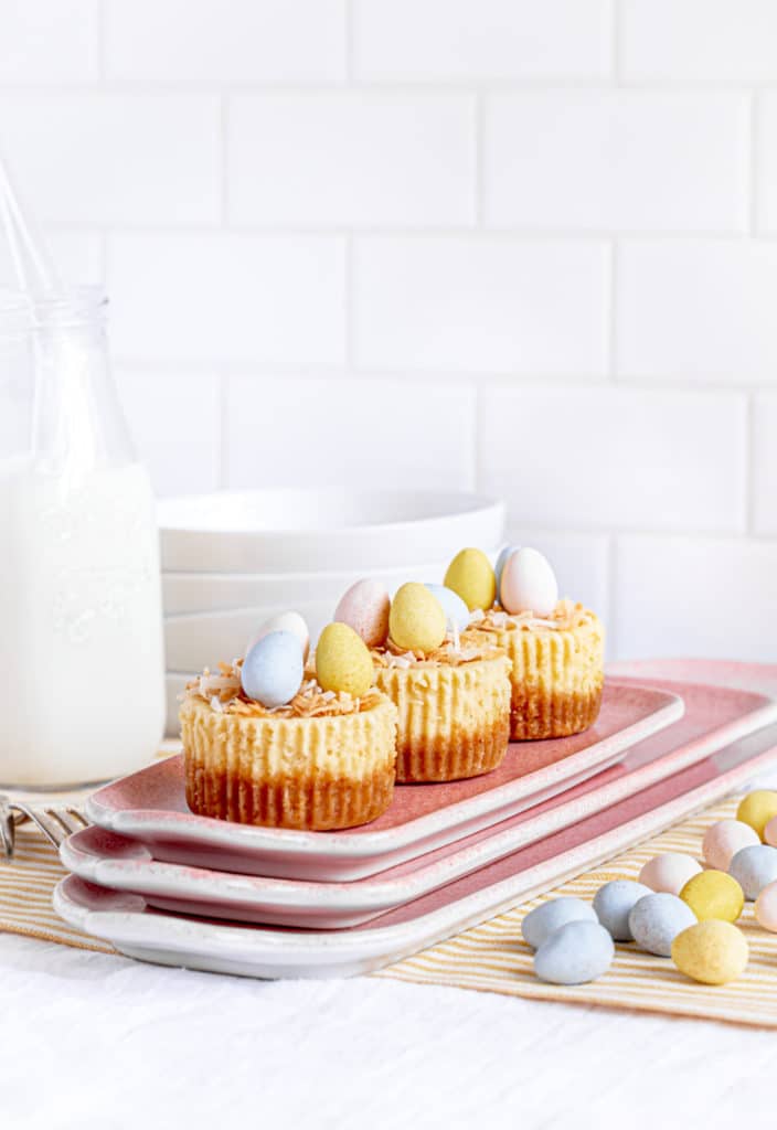 Three mini Easter cheesecake bites on a stack of small pink platters next to Cadbury eggs.