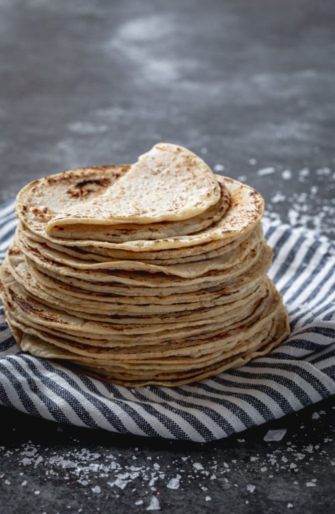 A stack of homemade corn tortillas on a blue/white striped kitchen towel.