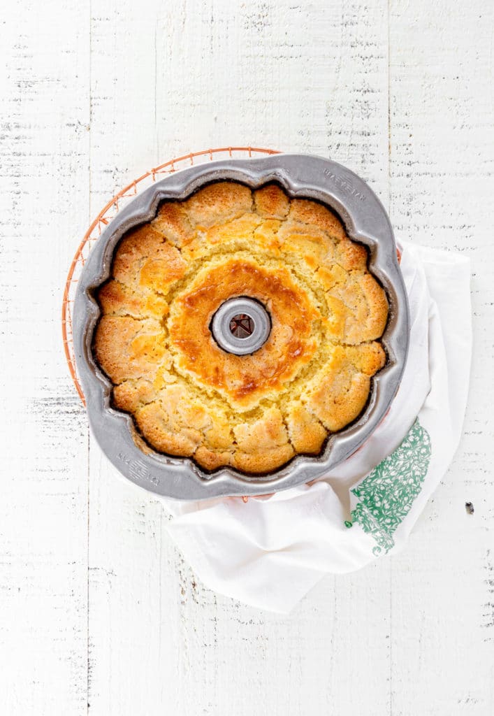 A lemon bundt cake cooling in the pan on top of a wire cooling rack.